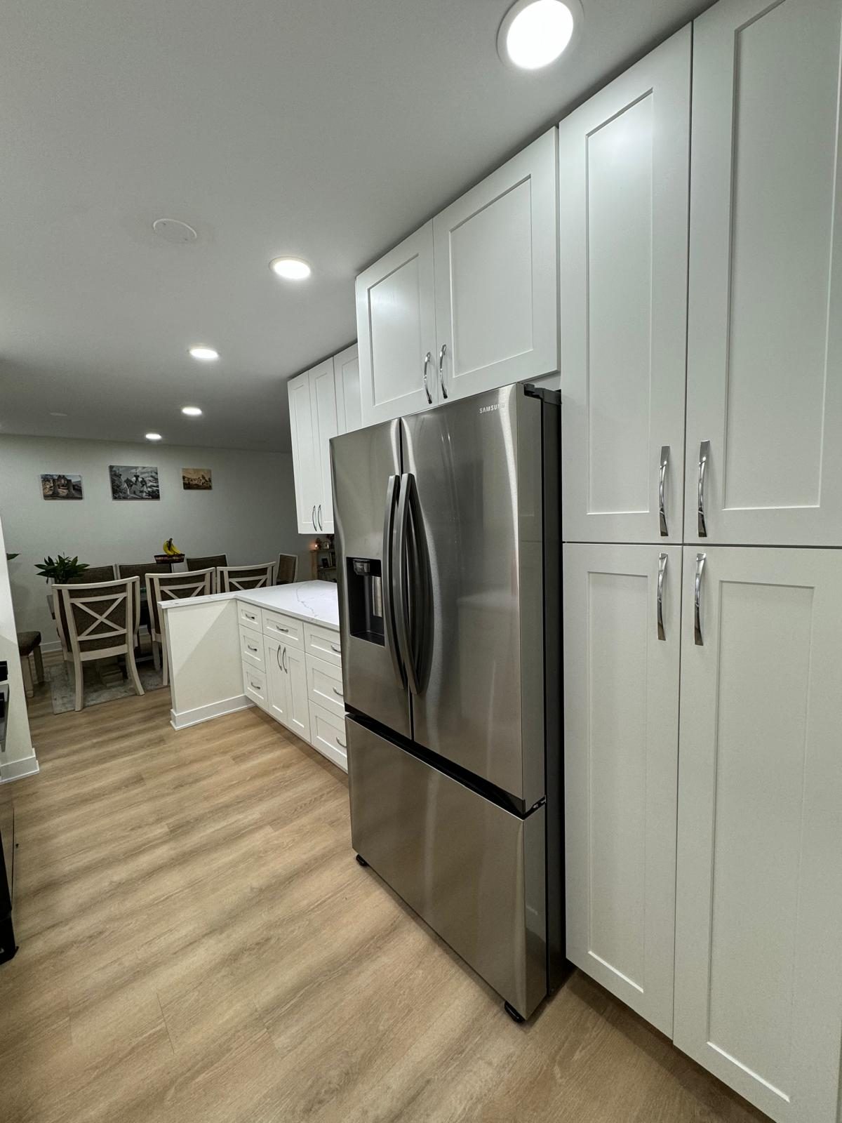 White floor-to-ceiling cabinets and pantry next to a stainless steel refrigerator